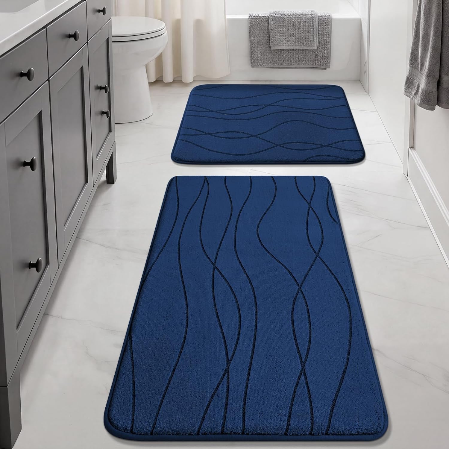 Long navy runner and square navy mat with subtle wave design laid out in a bright white bathroom.