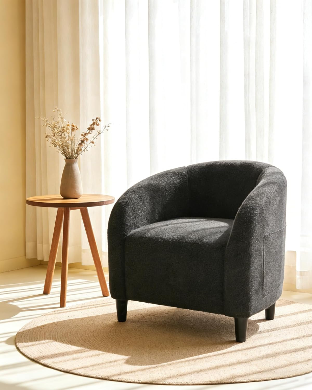 Single charcoal boucle barrel chair on a round rug beside a small wooden tripod table and vase.