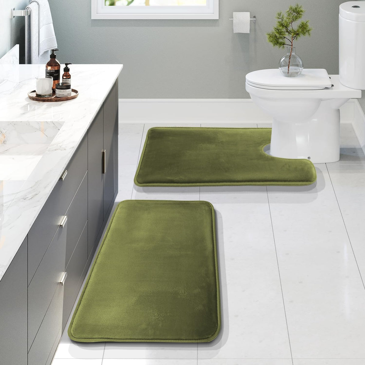 Bright bathroom with three olive-green memory foam rugs placed near the vanity and U-shaped toilet mat.