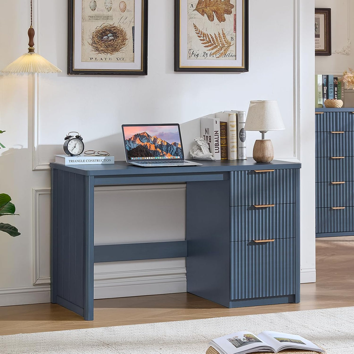 Blue wood desk with three fluted drawers and laptop, lamp, books on top in a styled room