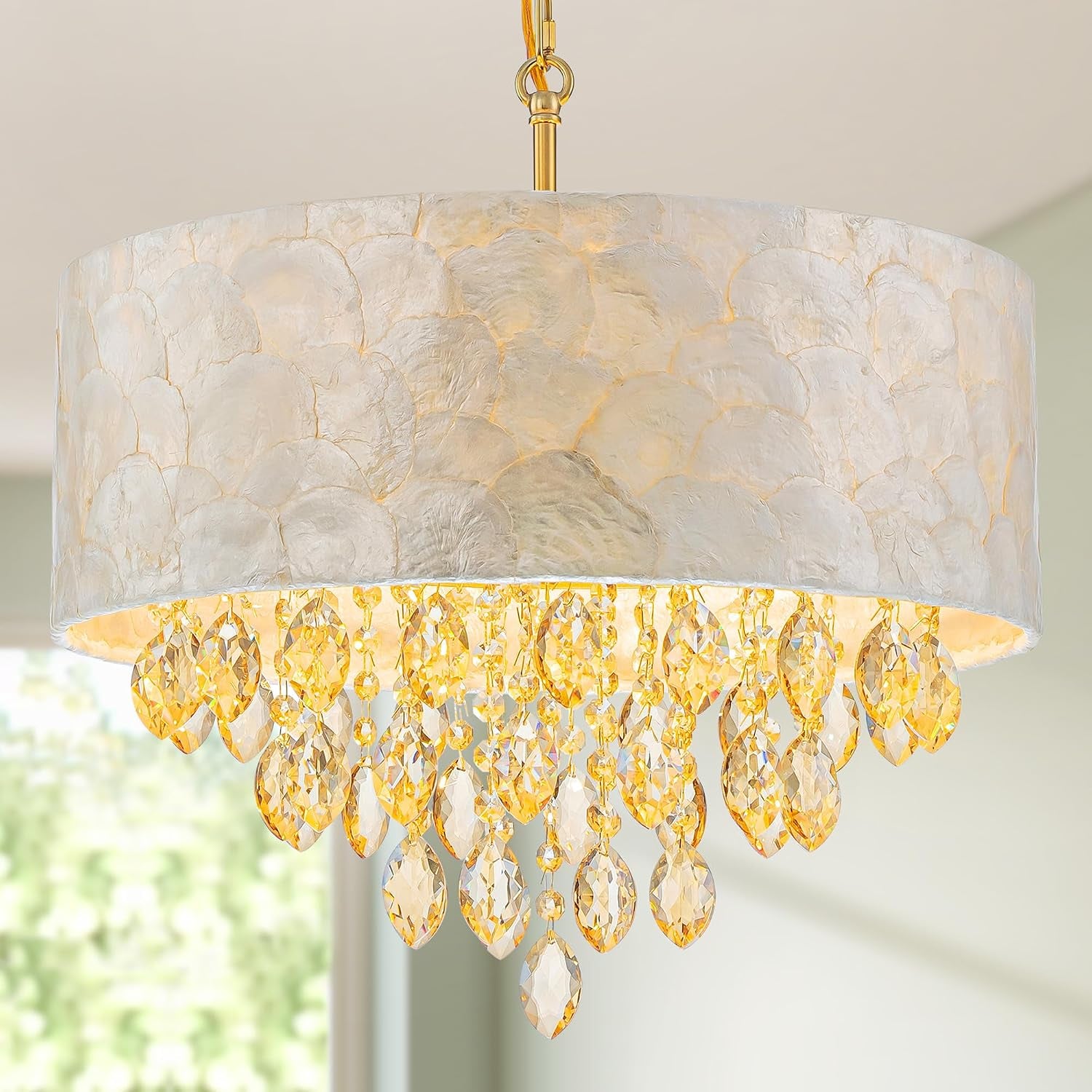 Low-angle close-up of a drum chandelier with layered capiz shade and dangling golden crystals.