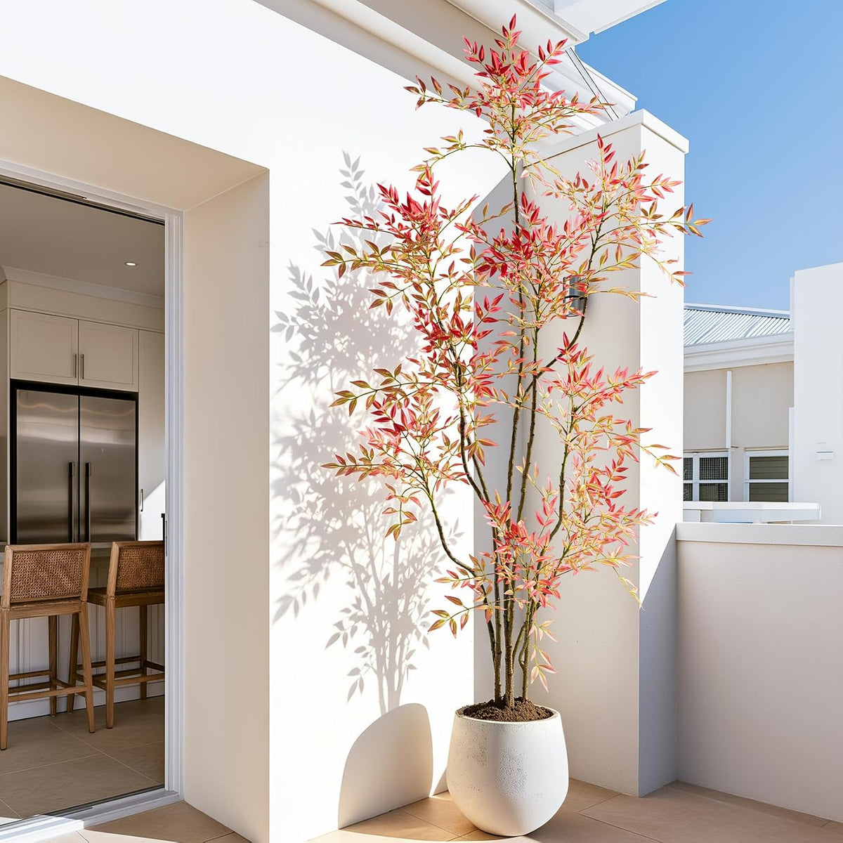 Faux Nandina with coral-red leaves in a white round planter on a sunny balcony, side profile