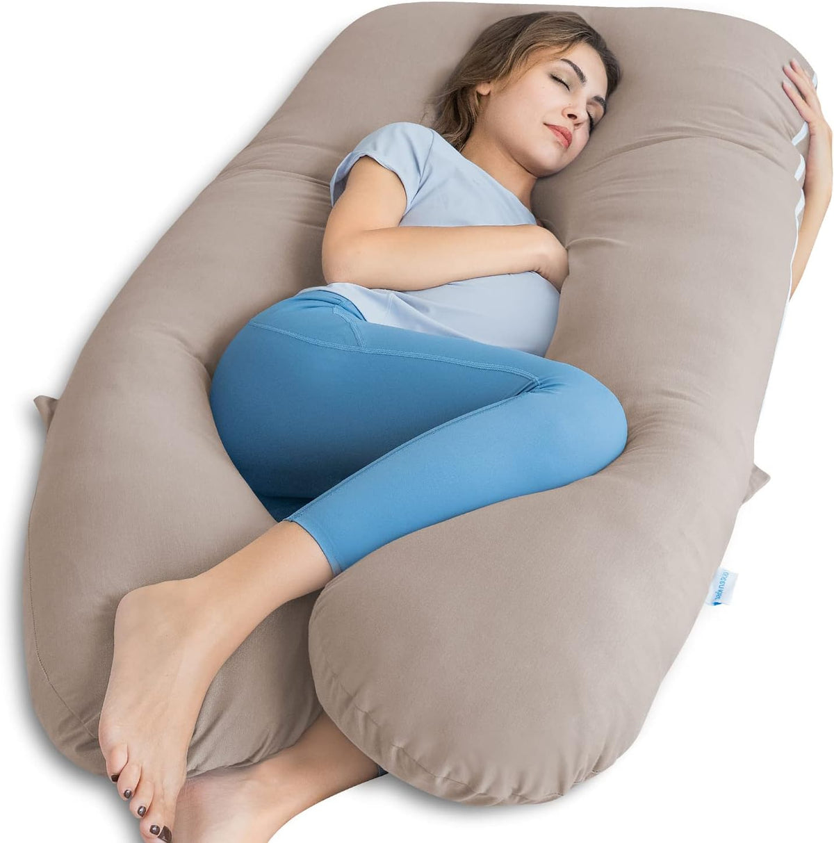 Angled view of a woman resting on a taupe U-shaped pregnancy pillow, legs curled and arms hugging the pillow.