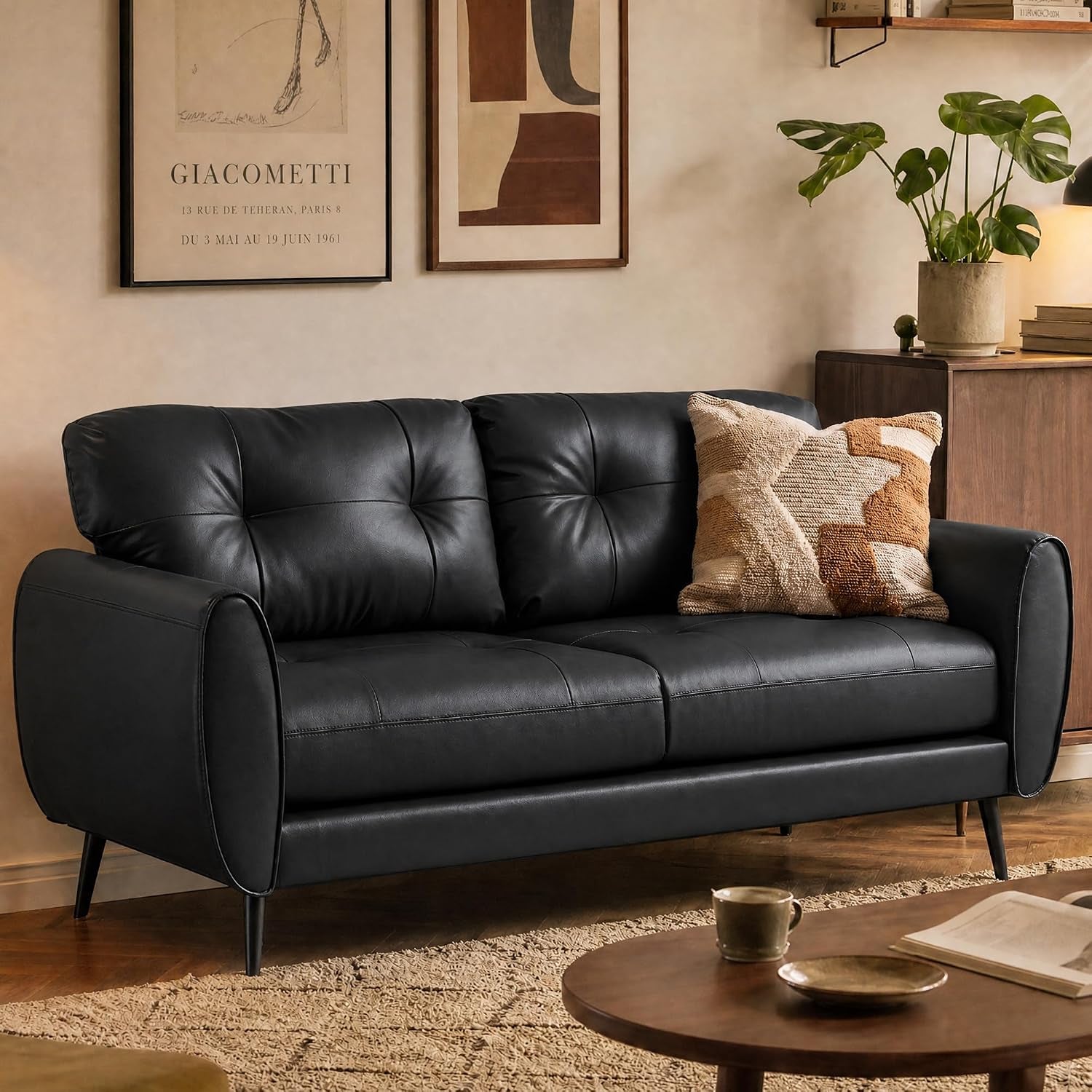 Black faux-leather loveseat in a cozy living room with tufted back, patterned cushion and round coffee table