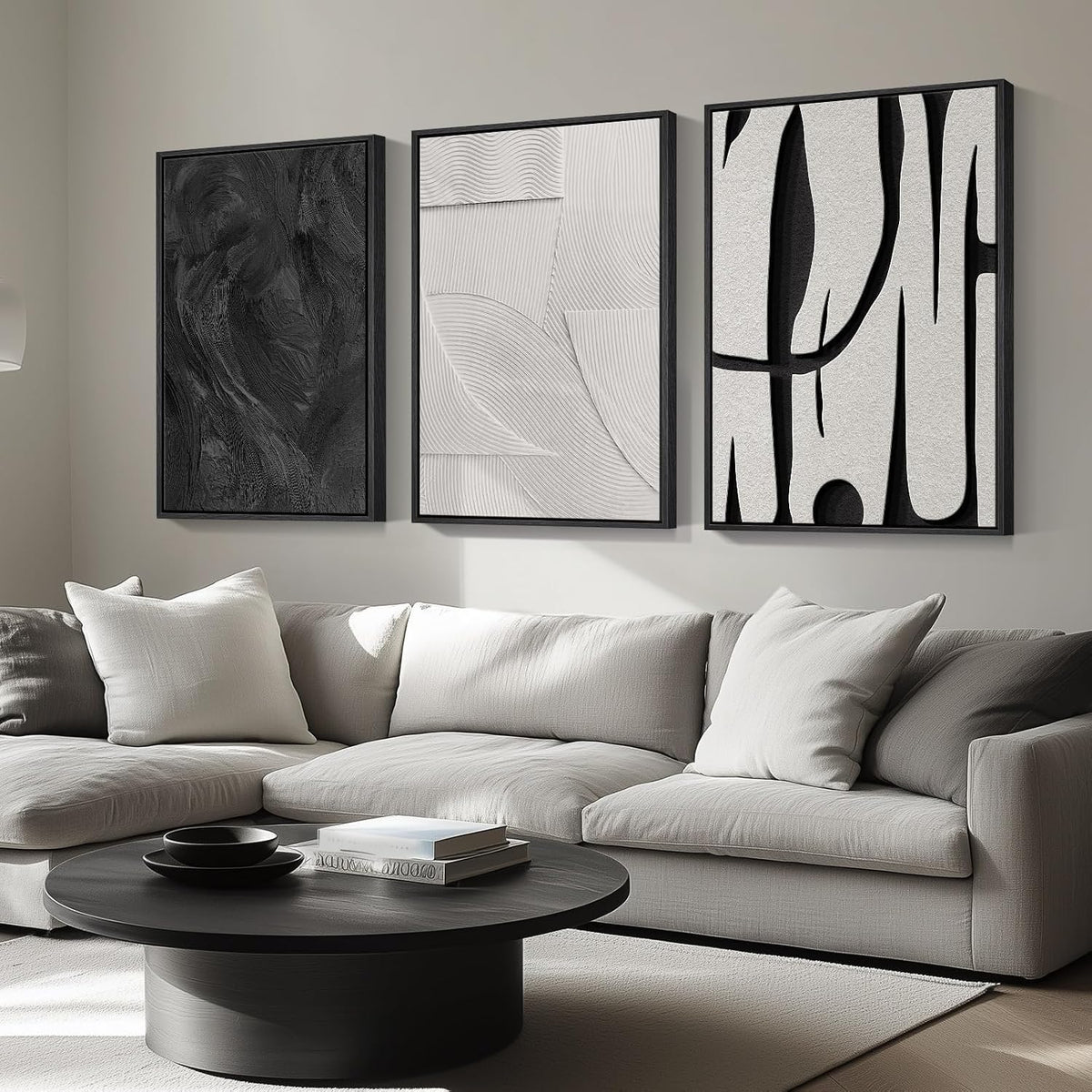 Three framed abstract panels in black, white, and gray shown angled above a light gray sectional sofa