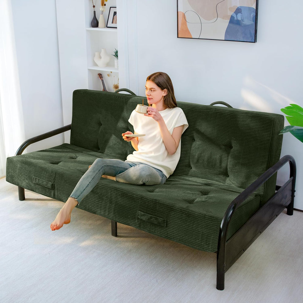 Dark green corded futon mattress set up as sofa on a black metal futon frame with a person sitting and holding a mug