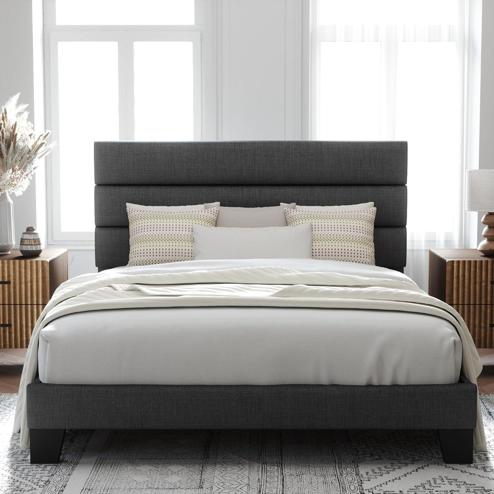 Front room view of a dark gray upholstered bed with a three-panel headboard, white bedding and black feet.