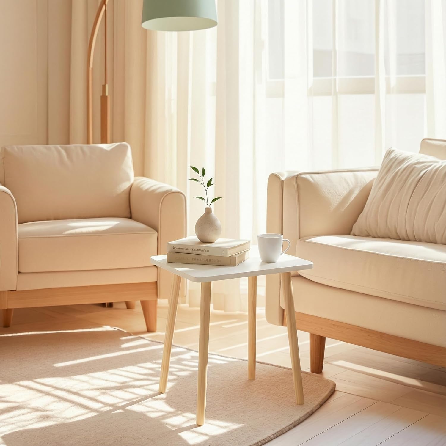 Small white side table with four light wooden legs placed between two cream armchairs, holding a vase, stacked books and a