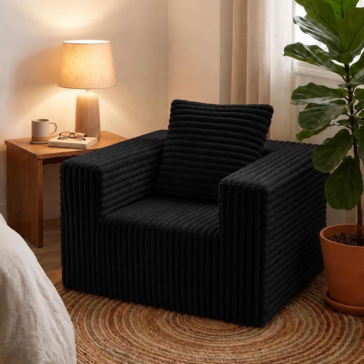 Black corduroy floor chair angled front view in a bedroom setting with a wooden side table and lamp