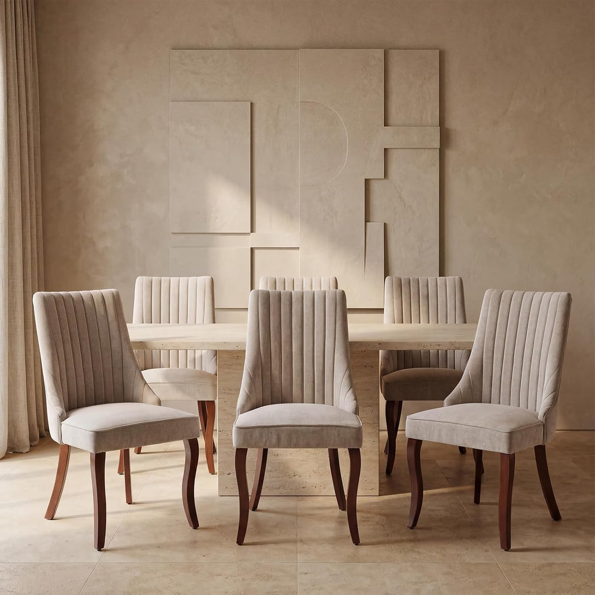Four beige upholstered high-back chairs with vertical channel tufting arranged around a light stone dining table.