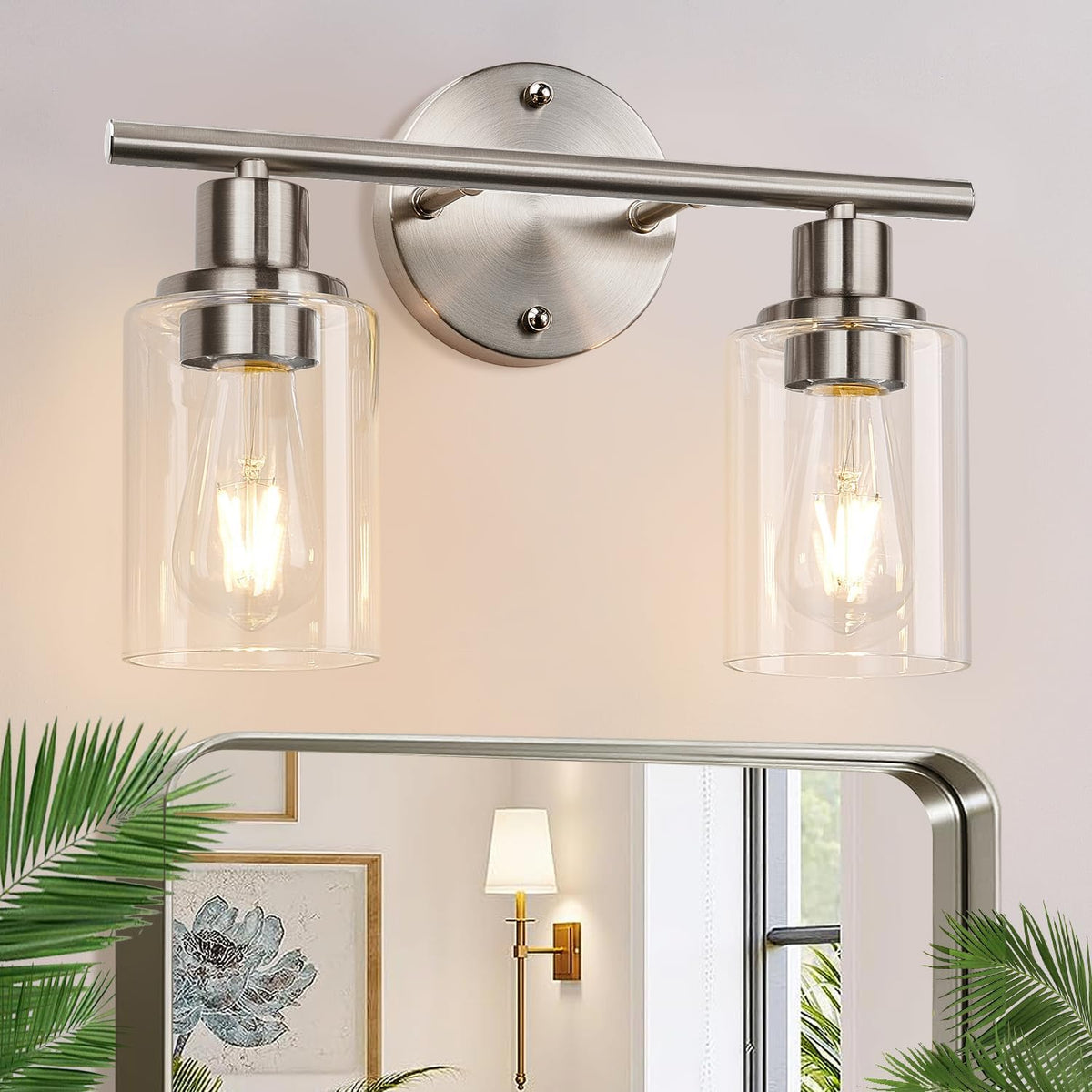 Close-up of two lit vanity bulbs with clear cylindrical shades and brushed nickel hardware above a mirror.