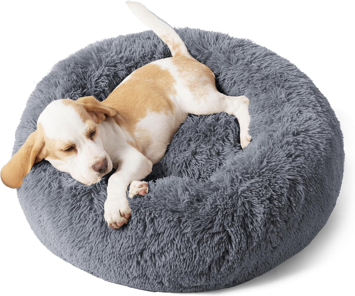 Top-side view of a gray fluffy round donut dog bed with a light tan-and-white puppy curled up sleeping.