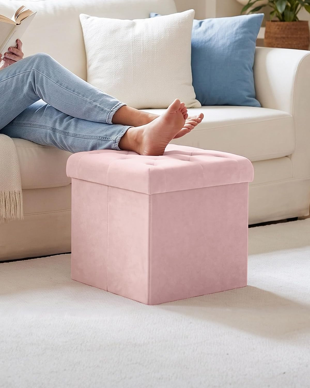 Pink velvet ottoman used as a footrest in front of a sofa with a person resting feet