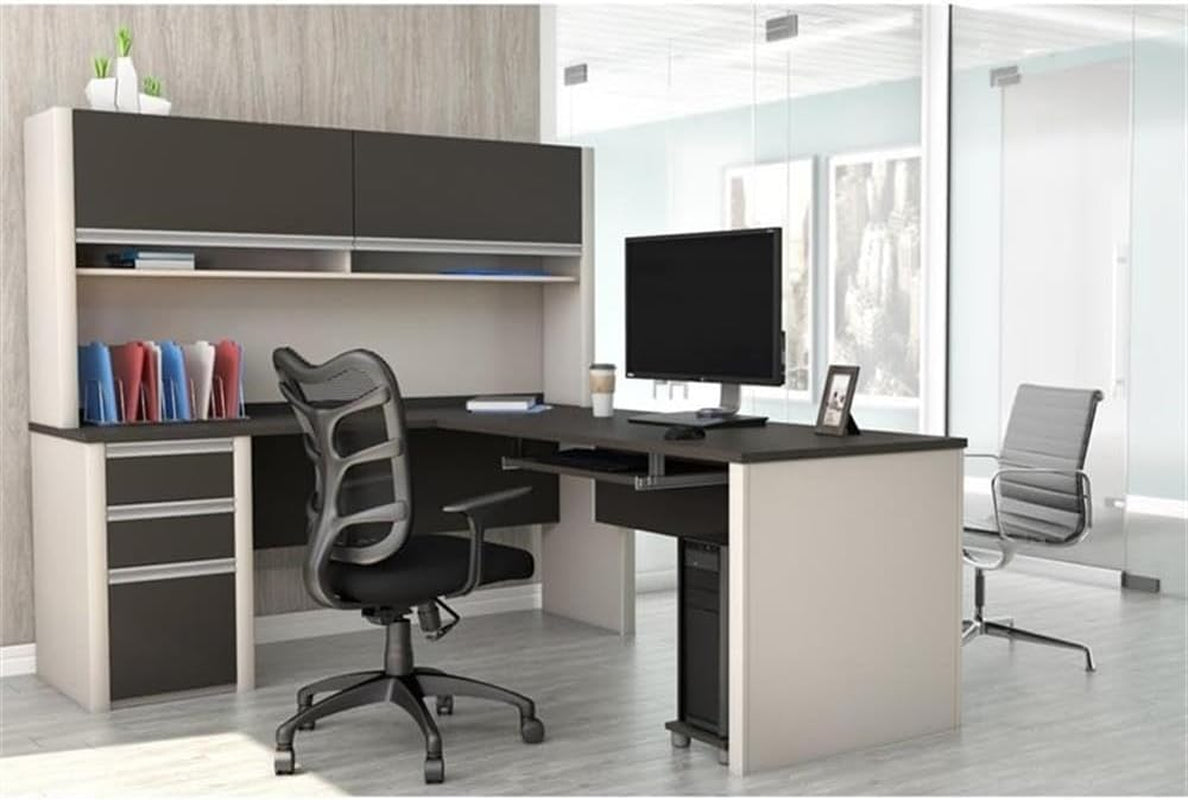 L-shaped office desk in sandstone and slate-gray placed in a glass-walled office with hutch, monitor, and task chair