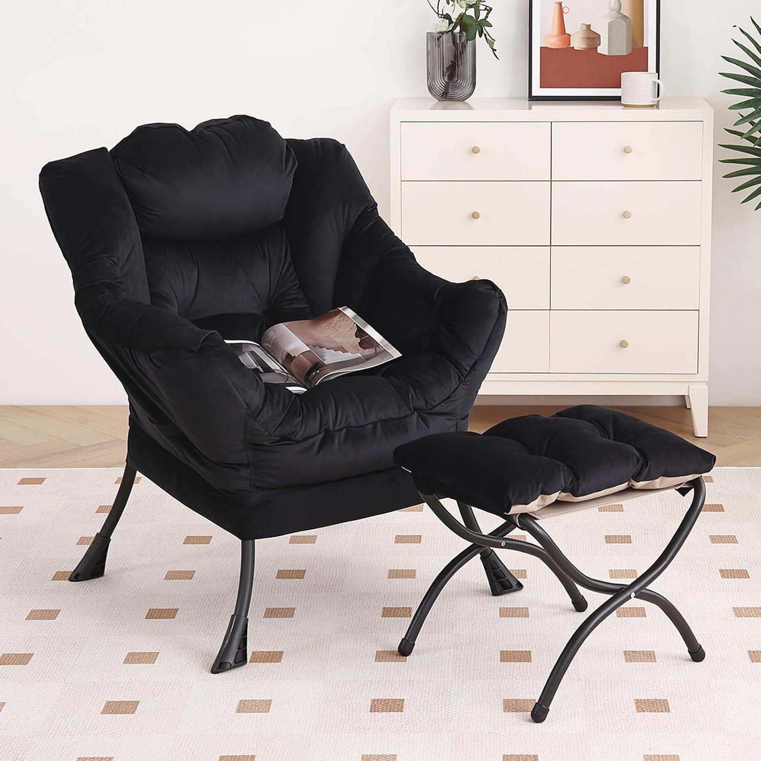 Black plush armchair with matching ottoman on patterned rug beside white dresser and decor