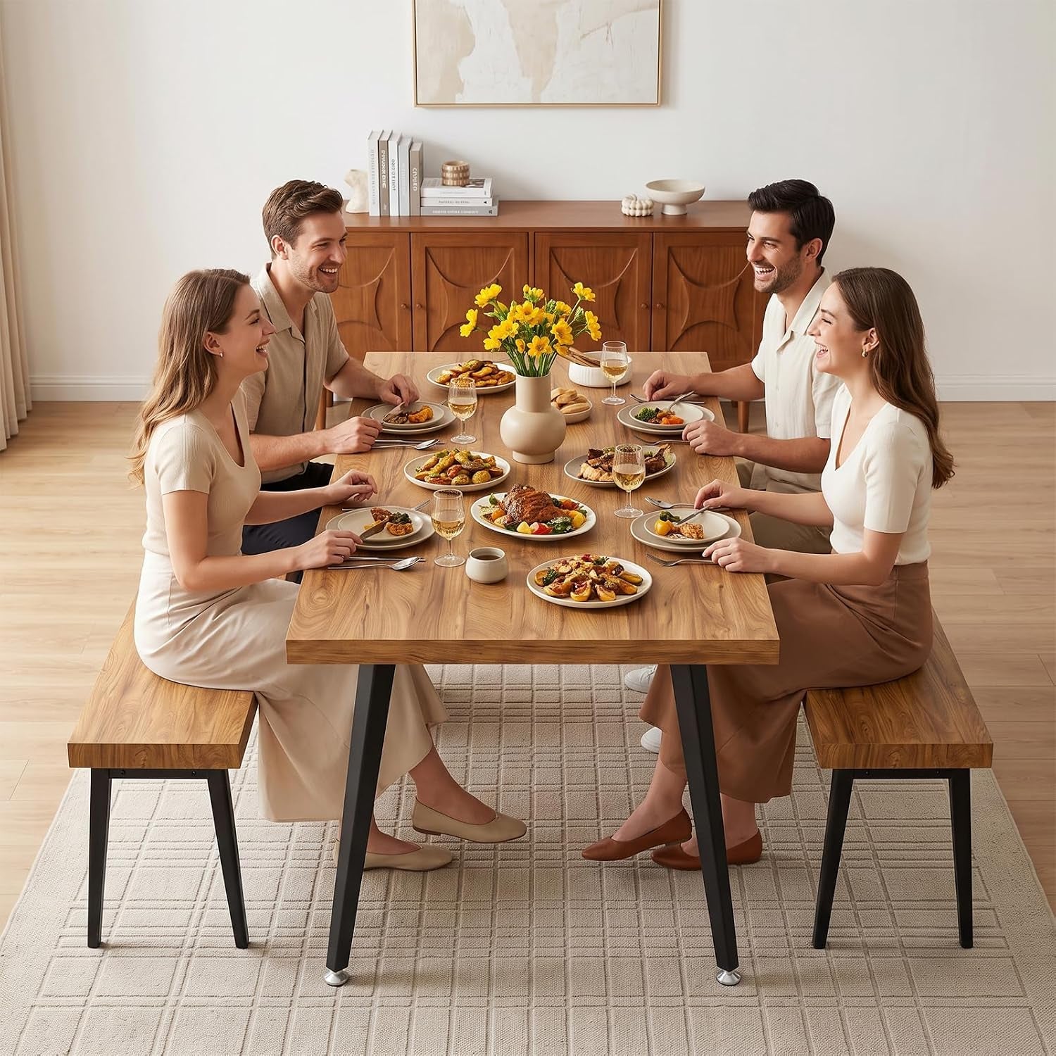 Four people dining at a wood table with matching benches, plates and a vase of yellow flowers in center.