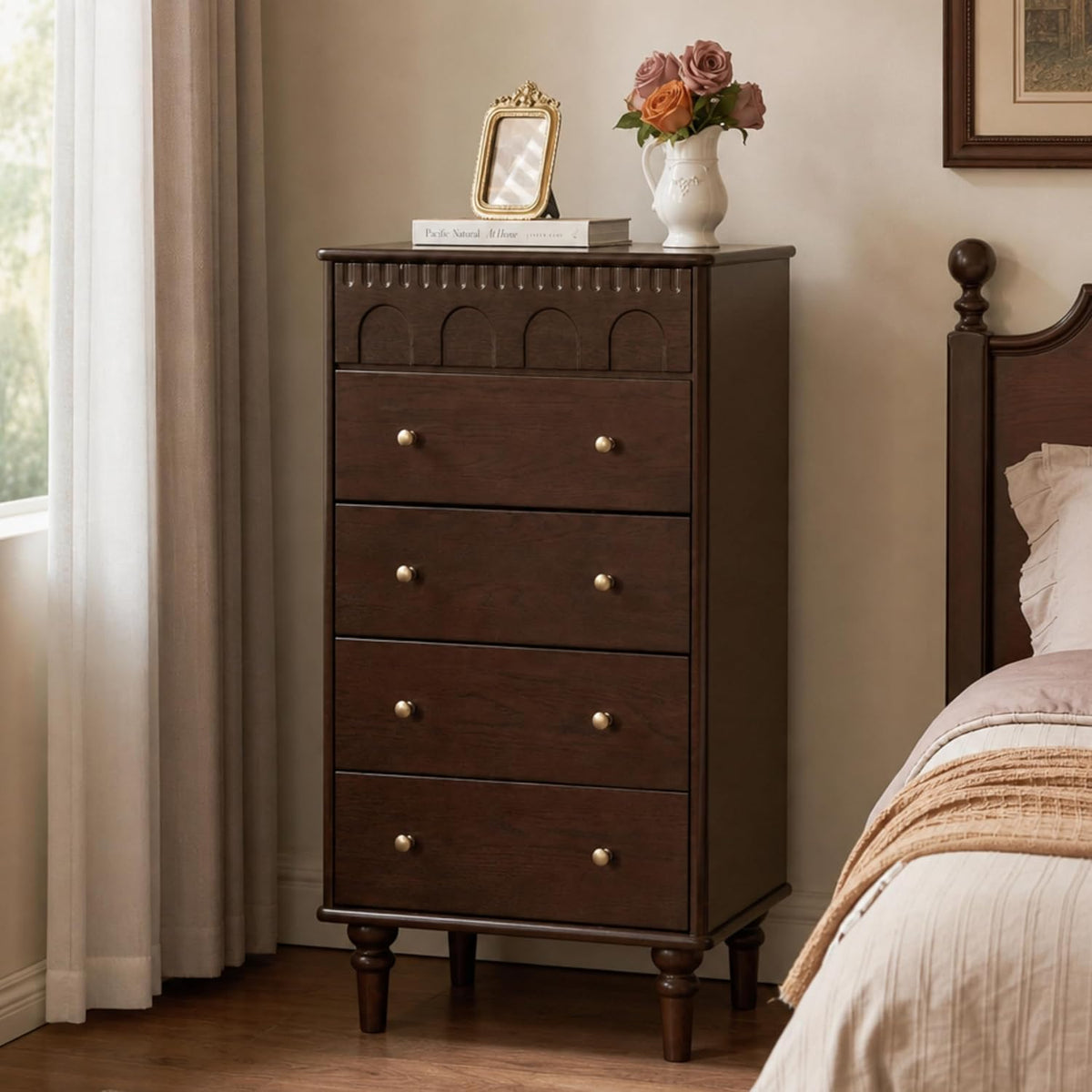 Tall dark wood five-drawer chest with turned legs beside a bed and curtains.