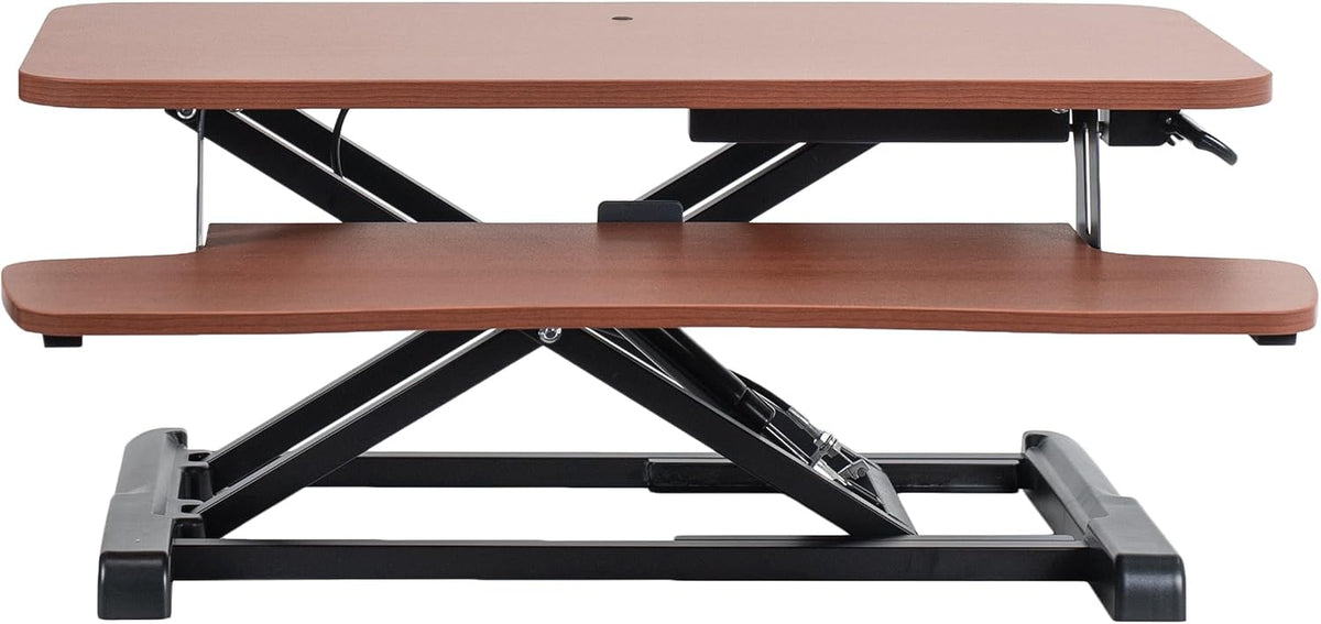 Side-on view of a cherry-finish standing desk converter with black metal scissor base.