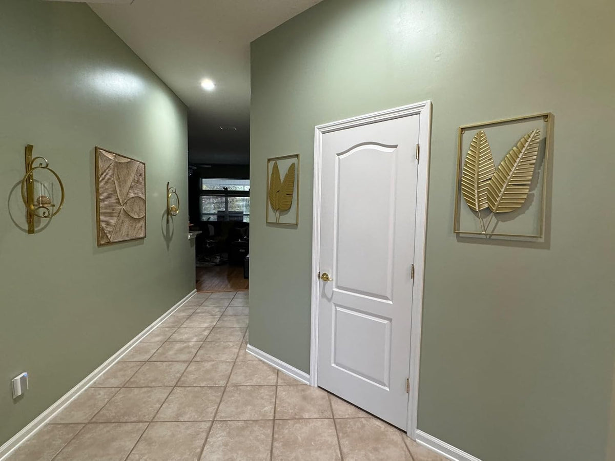 Hallway view with two gold leaf metal wall hangings mounted on a green wall beside a white door
