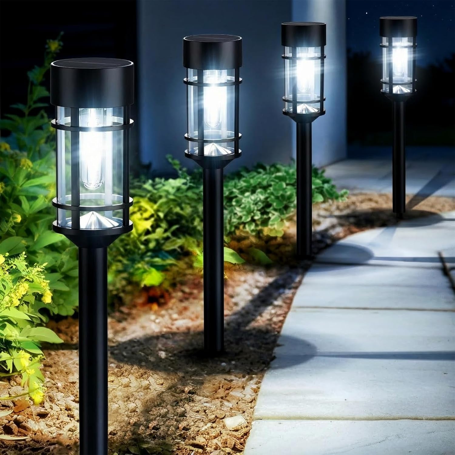 Row of lit black solar stake lights lining a garden path at night.