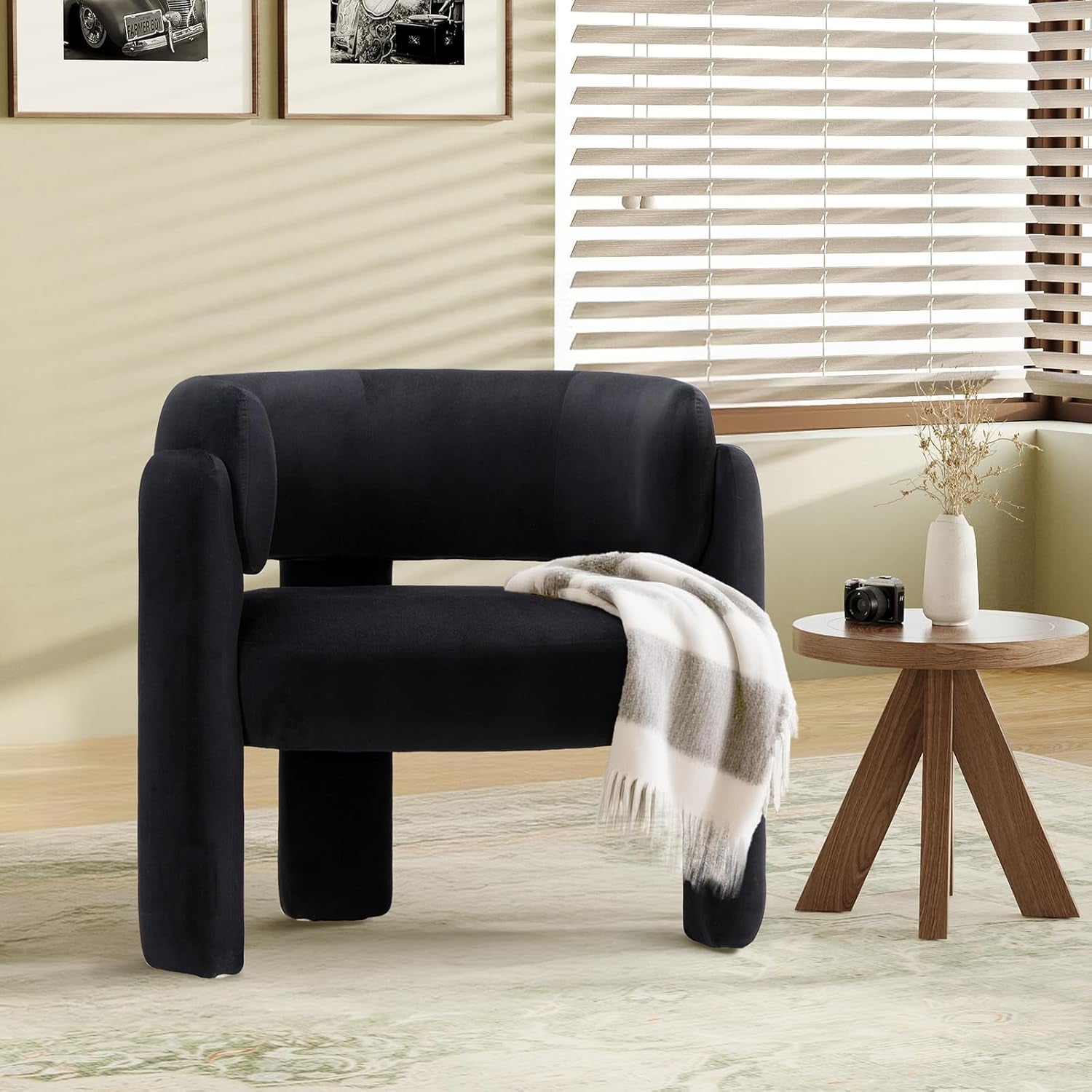 Black velvet barrel chair with a plaid throw on the seat beside a round wood accent table