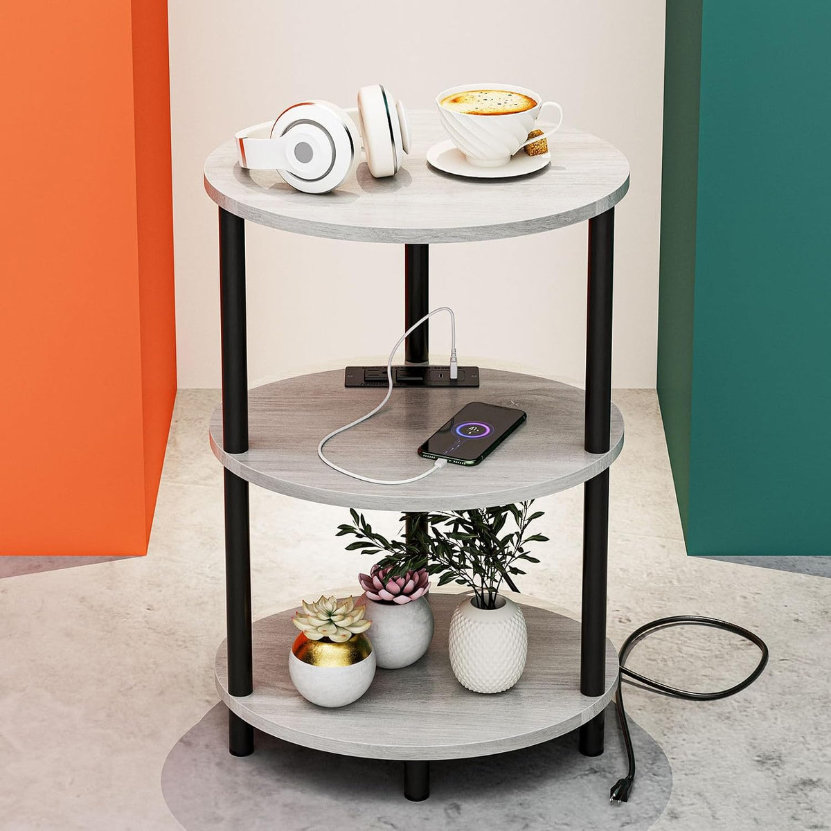 Round three-tier end table with light gray wood-look tops and black legs, phone charging on middle shelf.