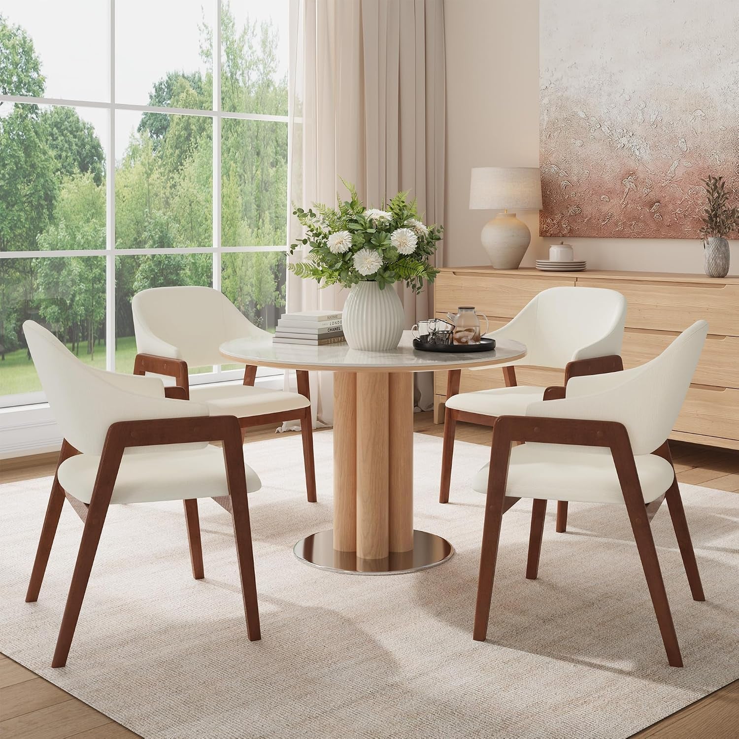 Four beige upholstered dining chairs around a round table beside a large window in a bright dining room