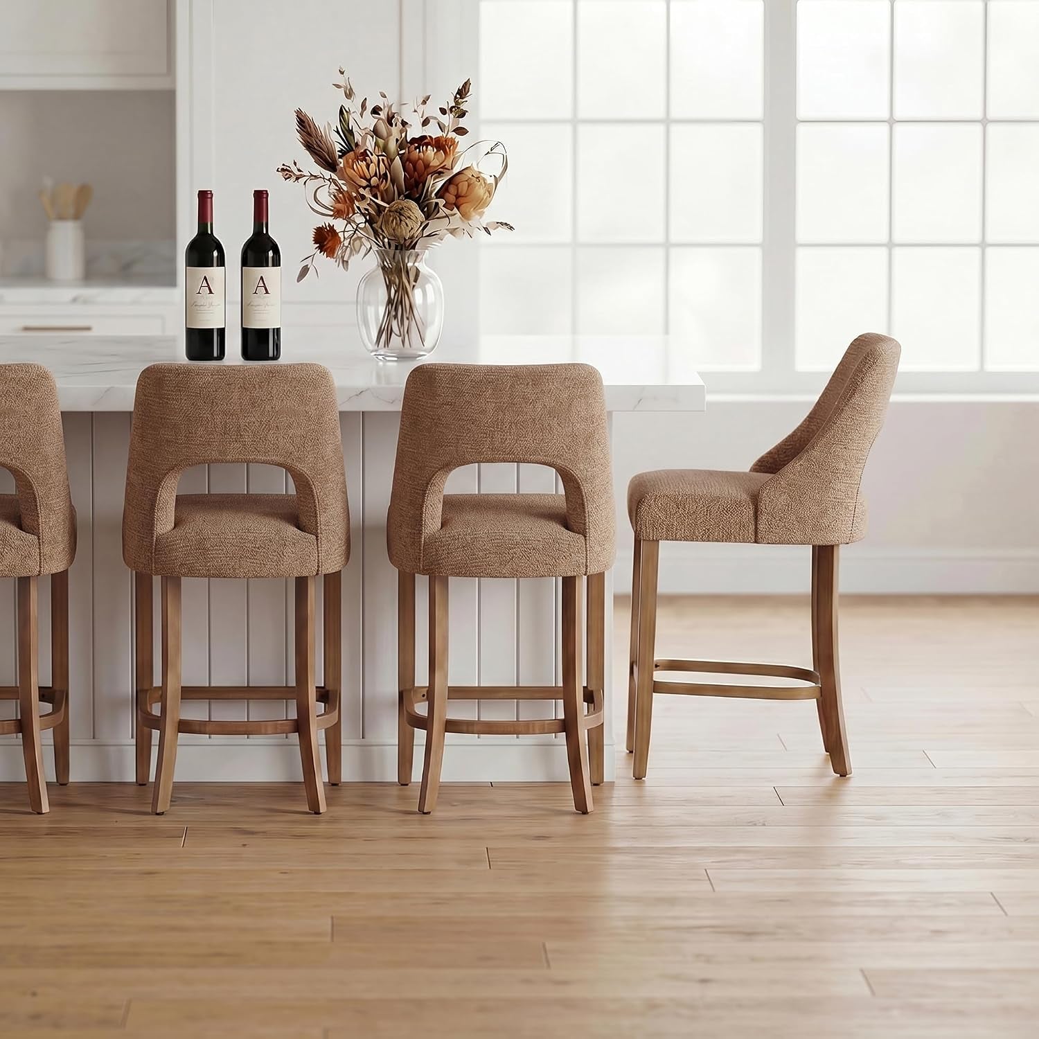 Three textured tan counter stools and one side view stool at an island with a vase and wine bottles.