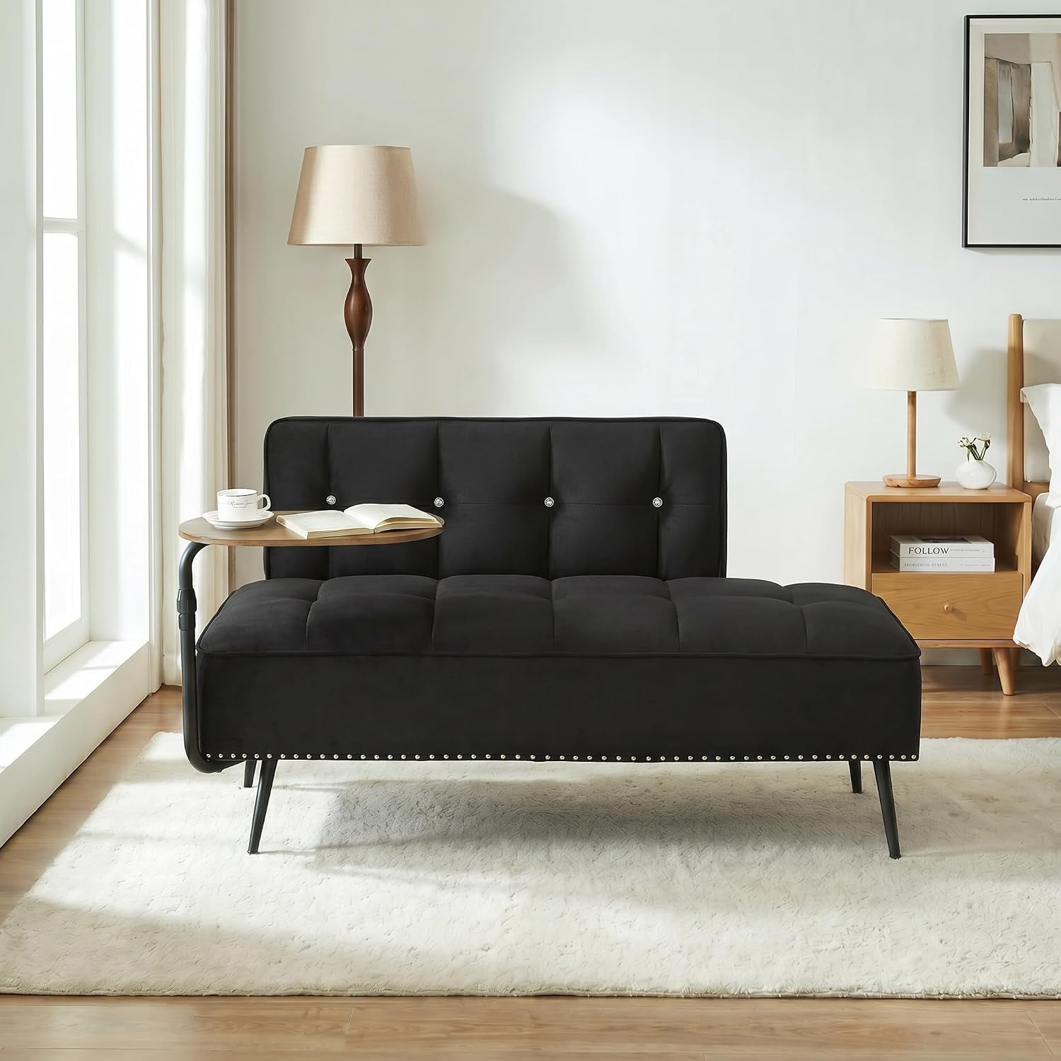 Black tufted convertible futon in a bright room with a small round side table attached on the left.