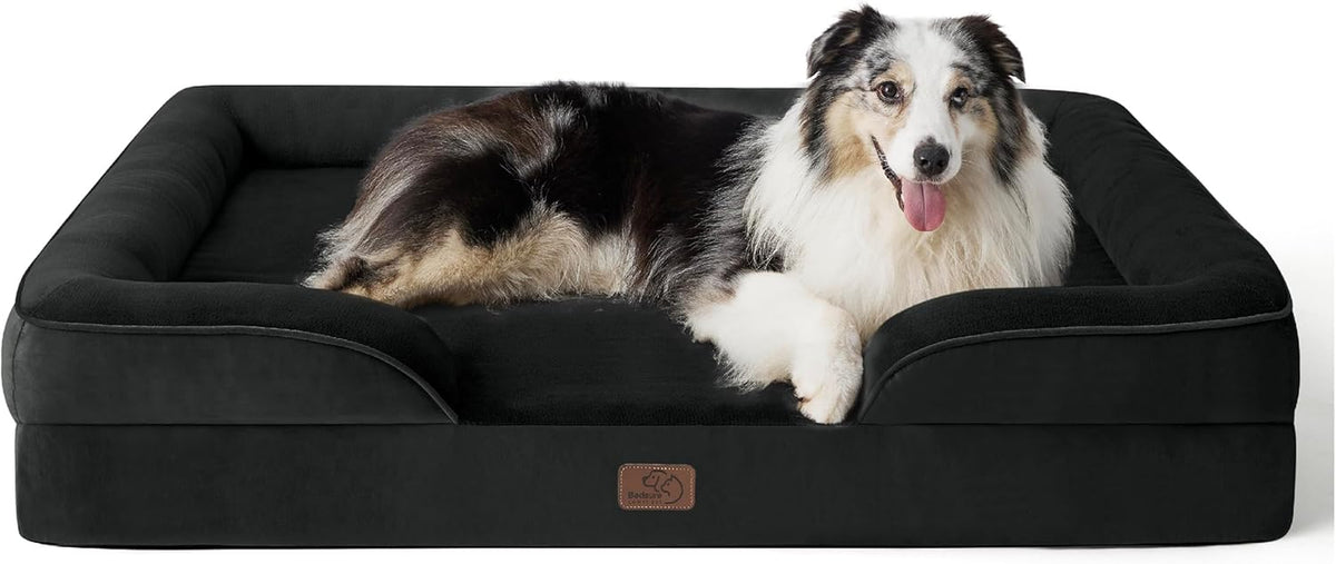 Black-and-white fluffy dog resting on a black rectangular bolster dog bed shown from the front.