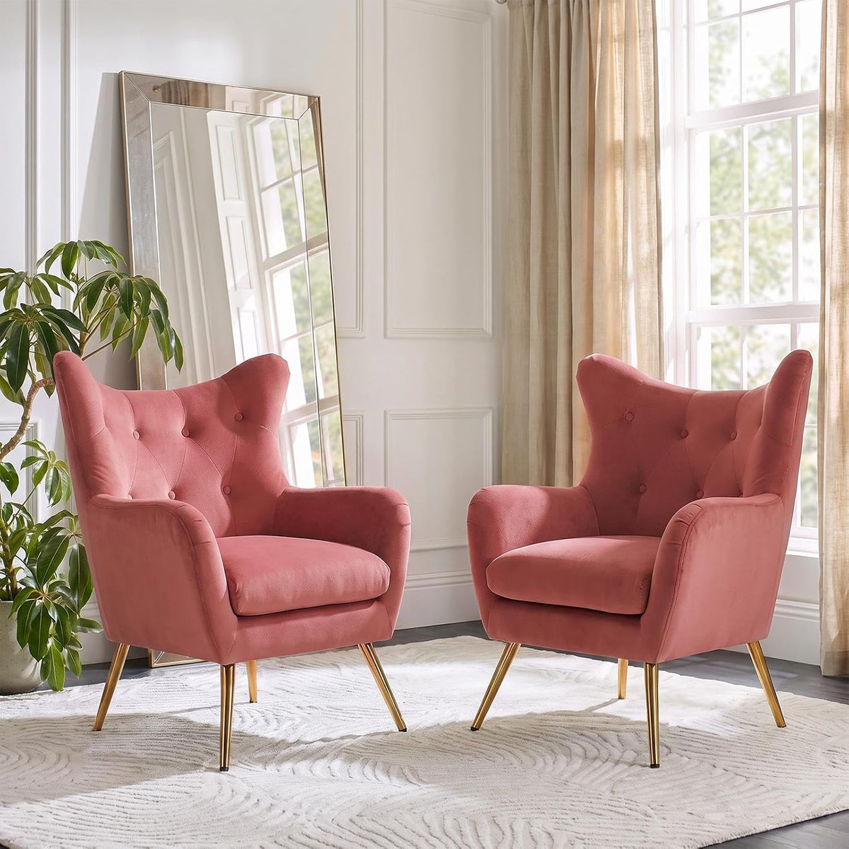 Pair of dusty-rose velvet wingback chairs with button tufting near a leaning floor mirror and houseplant.