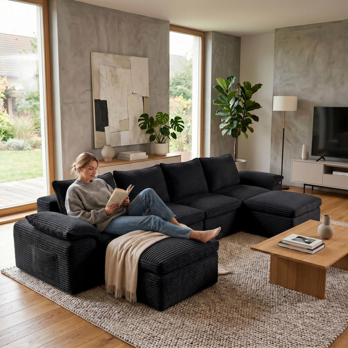 Black ribbed modular sectional with ottoman; a woman lounges reading on the chaise in a cozy living room.