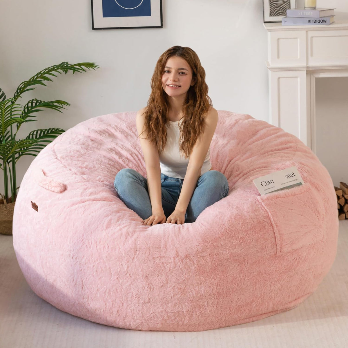 Woman seated cross‑legged in a blush pink bean bag with a folded magazine tucked into the pocket at her side.