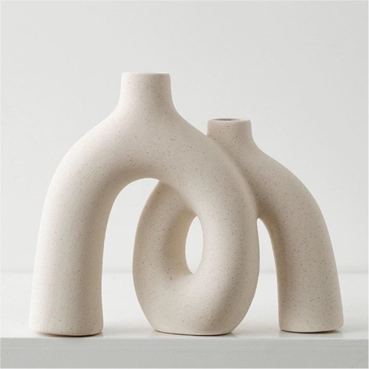 Cream ceramic hollow-center donut vase viewed front-left close-up on a white surface with textured finish