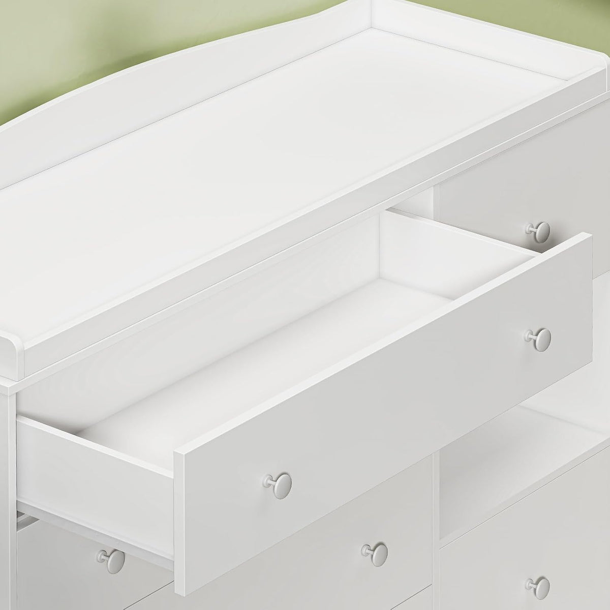 Close-up detail of the dresser's top changing surface and an open upper drawer with round knobs.