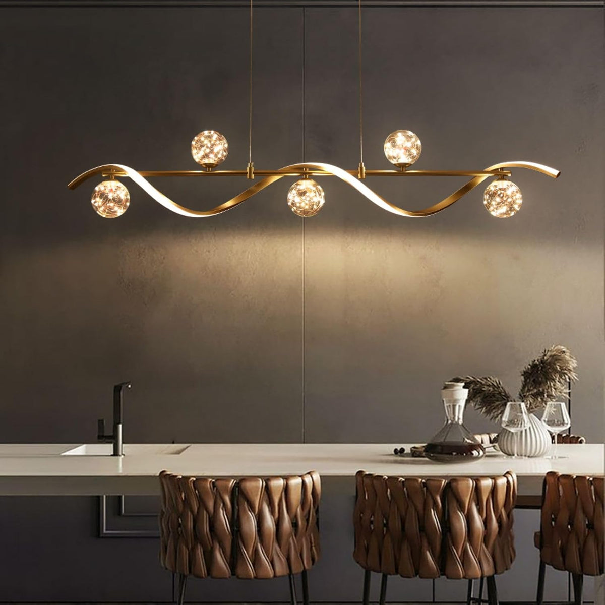 Centered view of gold linear chandelier lit against a dark wall highlighting curved metal wave and glass globes
