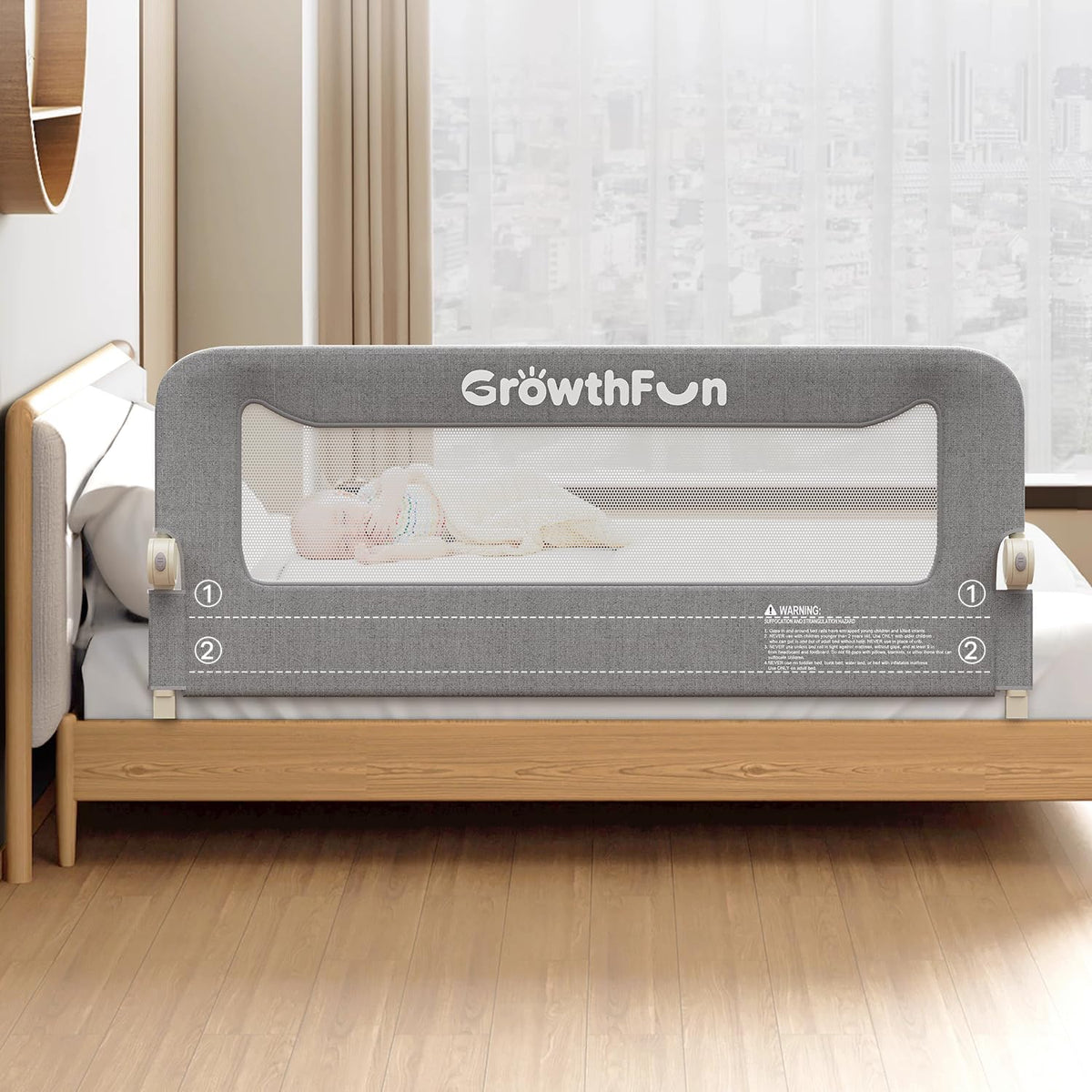 Front view of a dark gray foldable toddler bed rail mounted on a wooden bed with sheer window behind