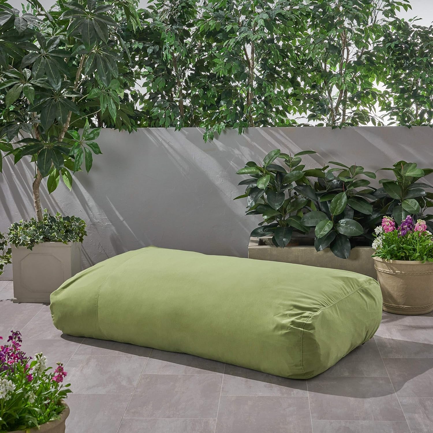 Empty green floor lounger placed on a tiled patio with garden planters in the background