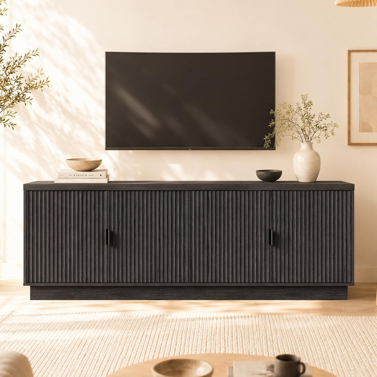 Low black media console with vertical fluted front panels beneath a wall-mounted TV in a warm room