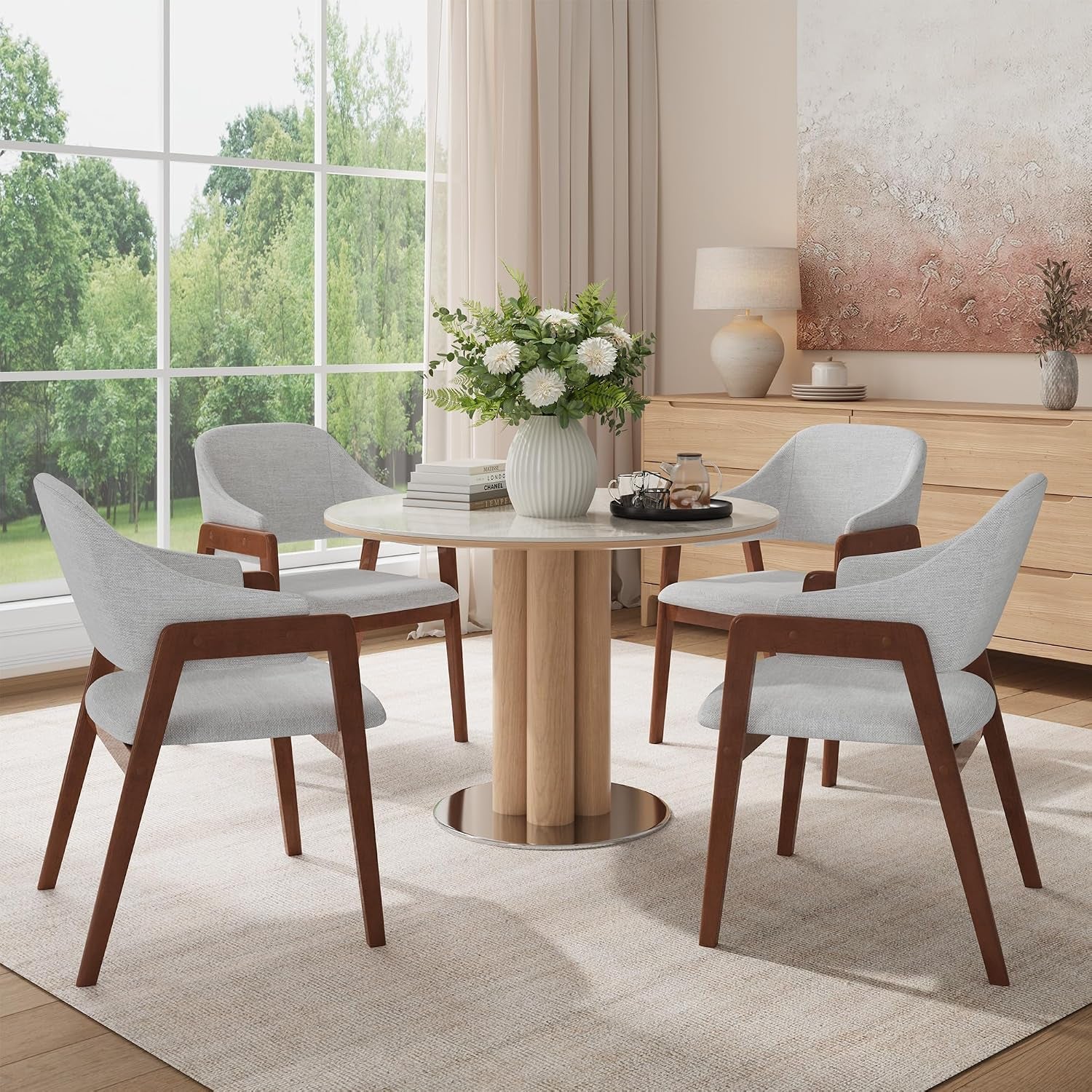 Four light-gray upholstered armchairs with walnut-tone frames around a round dining table by a large window.