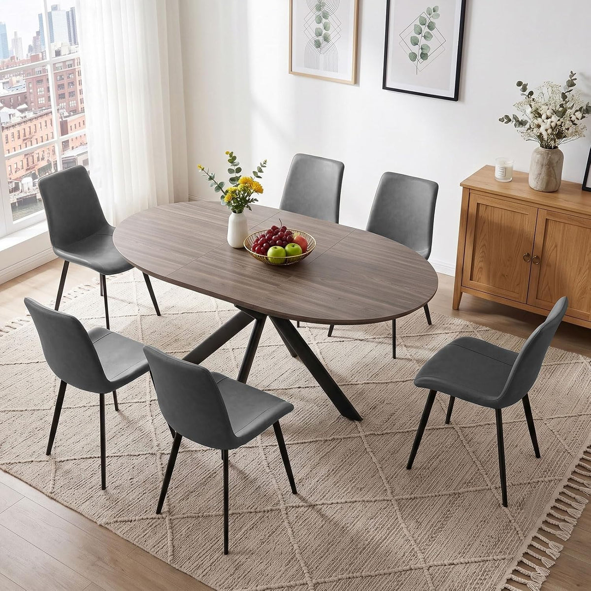Oval wood dining table with four gray upholstered chairs in a bright dining room.