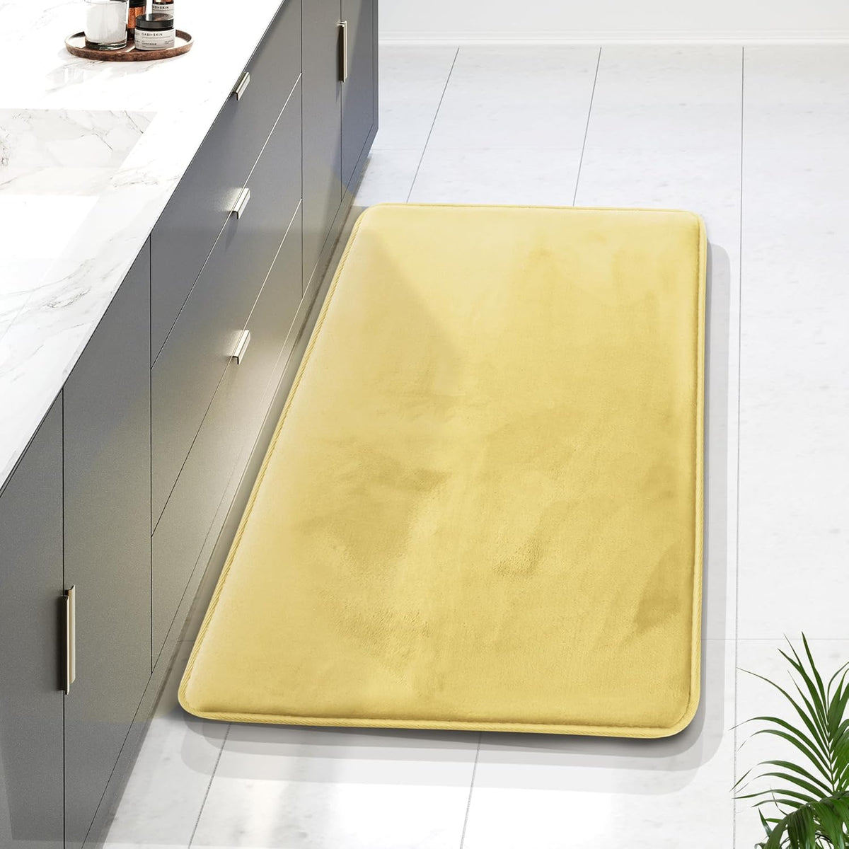Overhead view of a long yellow runner mat beside a gray vanity on white tile, showing plush surface and piped edges.