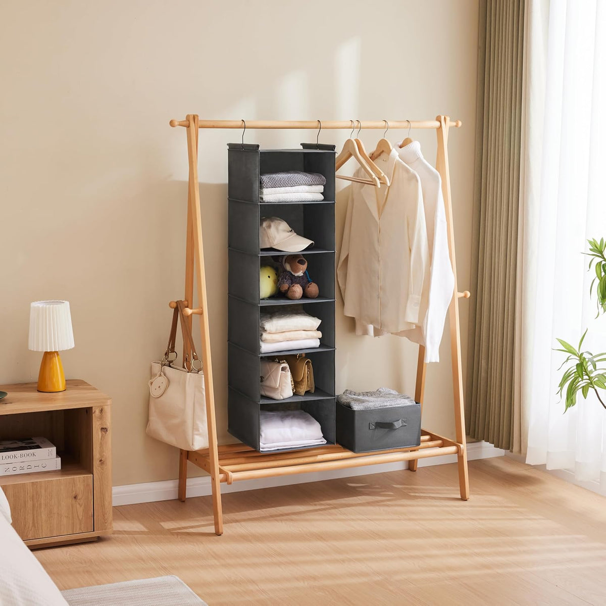 Grey 6-tier hanging organizer on a wooden rack beside hanging shirts and a bedside table