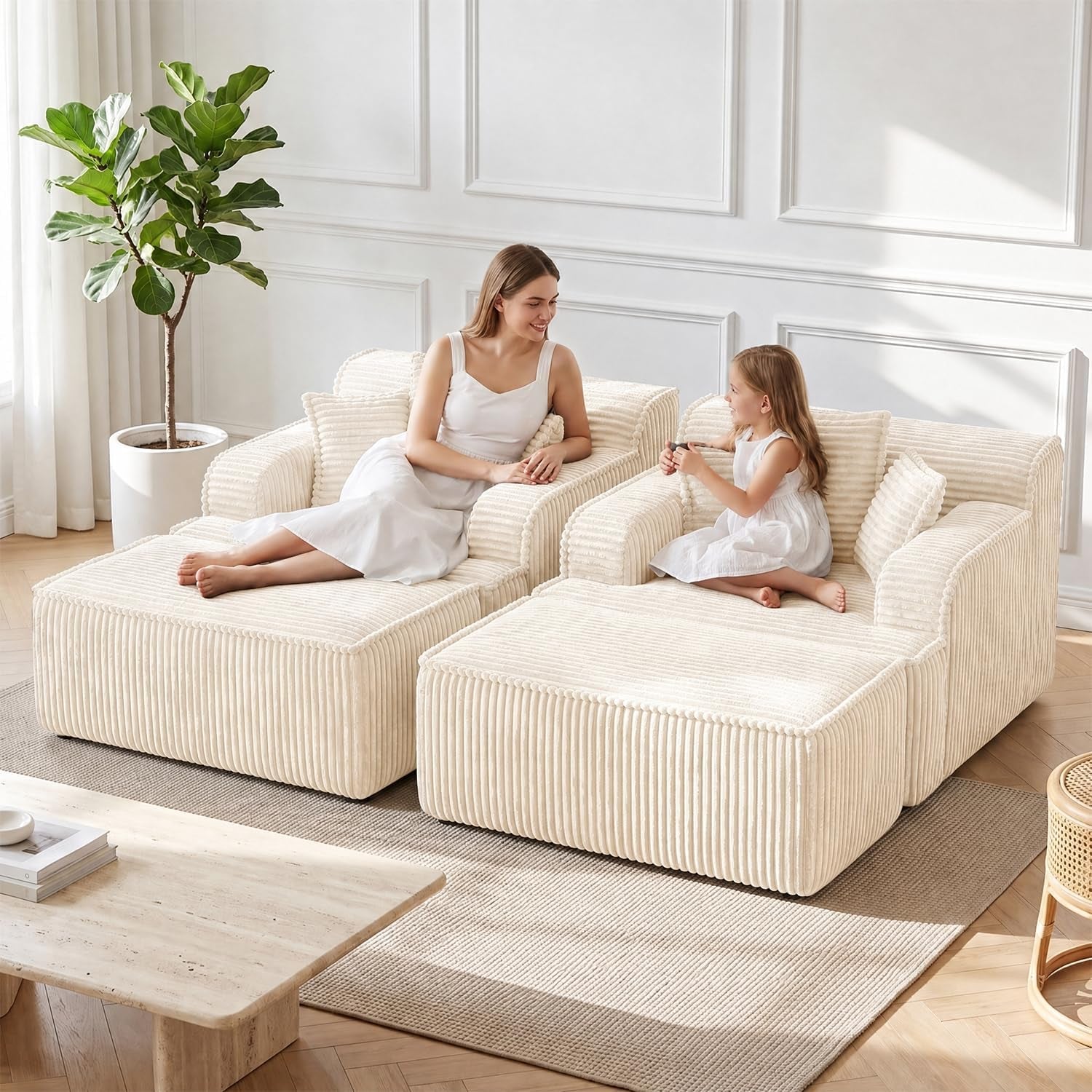 Woman and young girl sitting on two beige corduroy chaise lounges with ottomans in a bright living room.