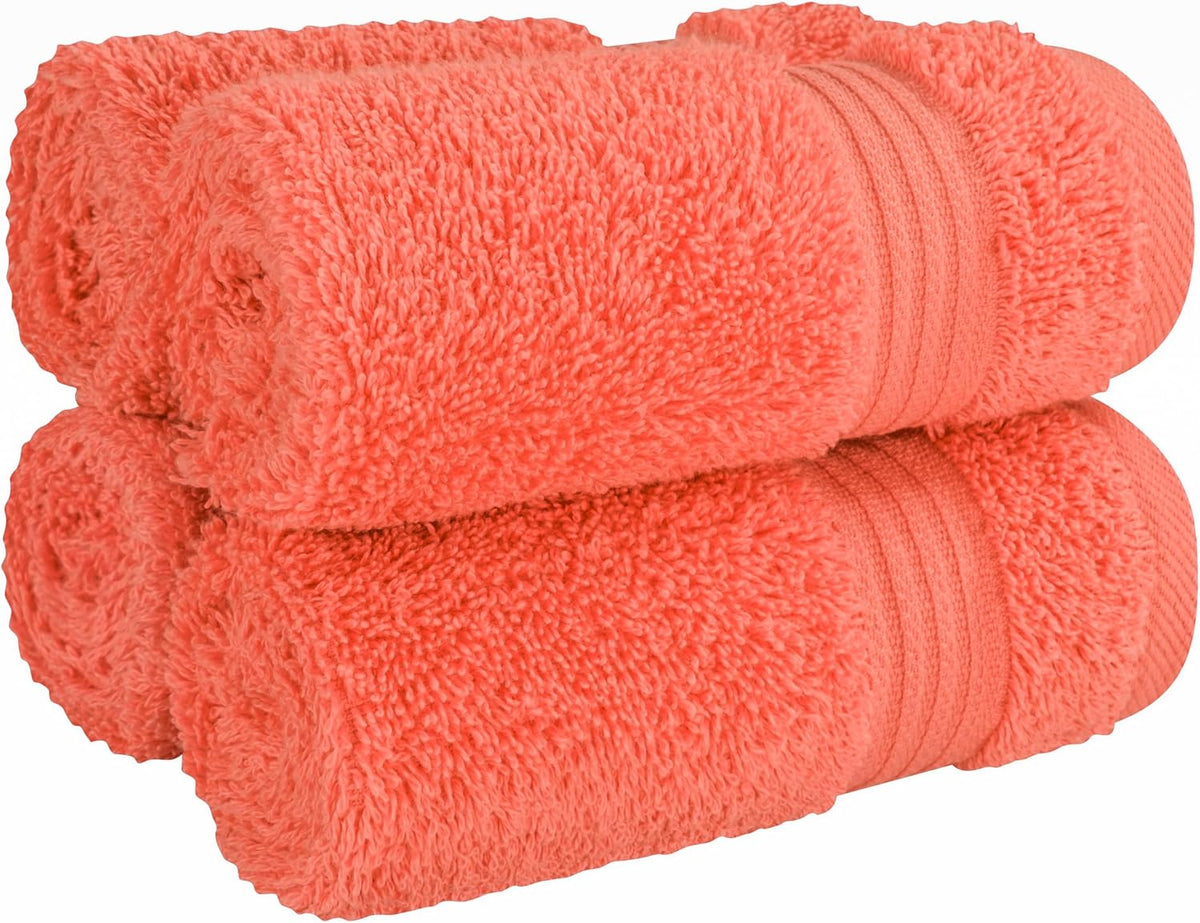 Close-up of four coral-orange towels rolled and stacked, highlighting plush pile and ribbed band.