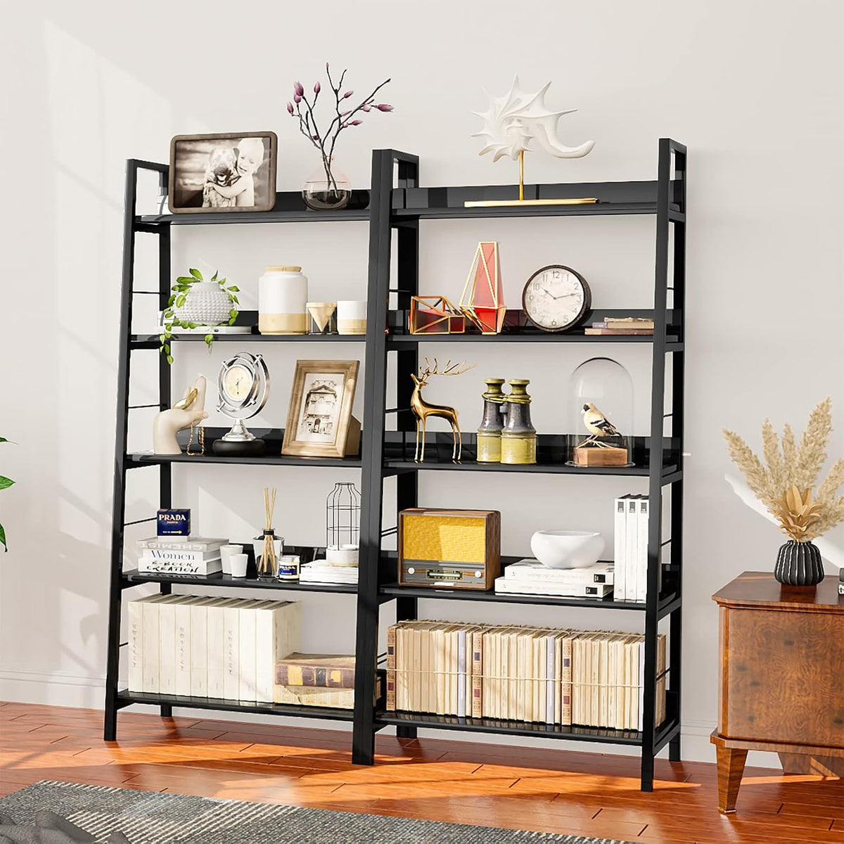 Angled close view of two black ladder-style 5-tier bookcases filled with decor and books