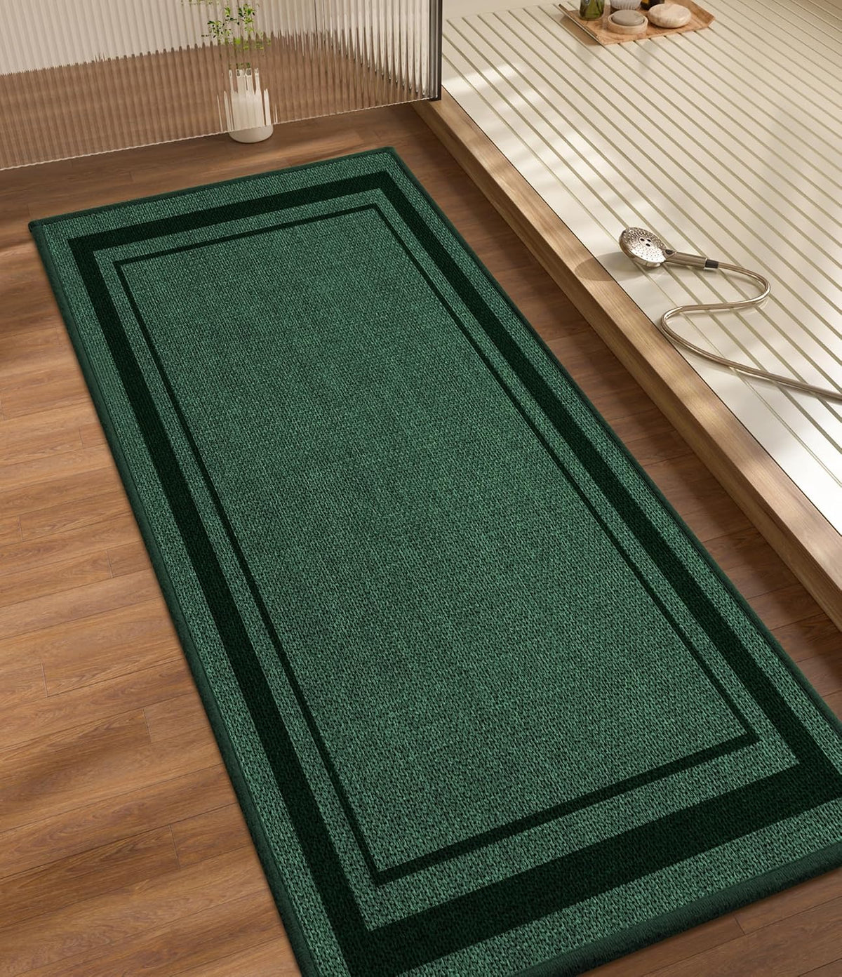 Long green runner-style bath mat with double border laid on wood flooring beside a tub platform