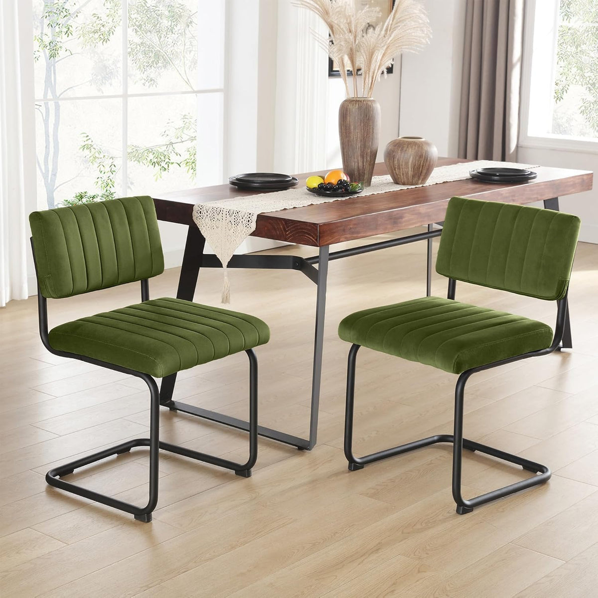 Two green velvet cantilever chairs in foreground with a wooden table, runner and vases centered behind them