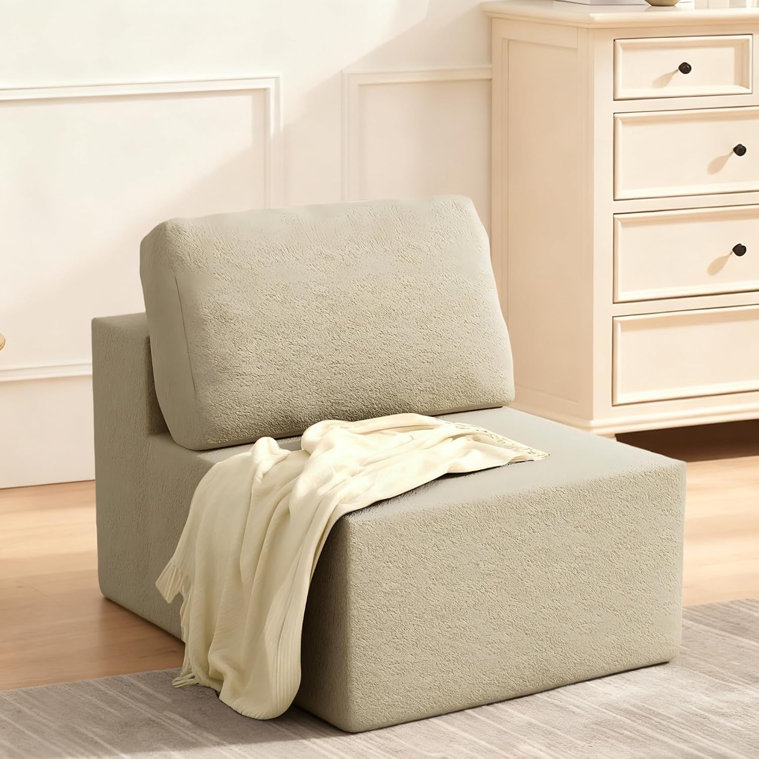 Side view of a single beige armless modular seat with back cushion and a cream throw draped over it.