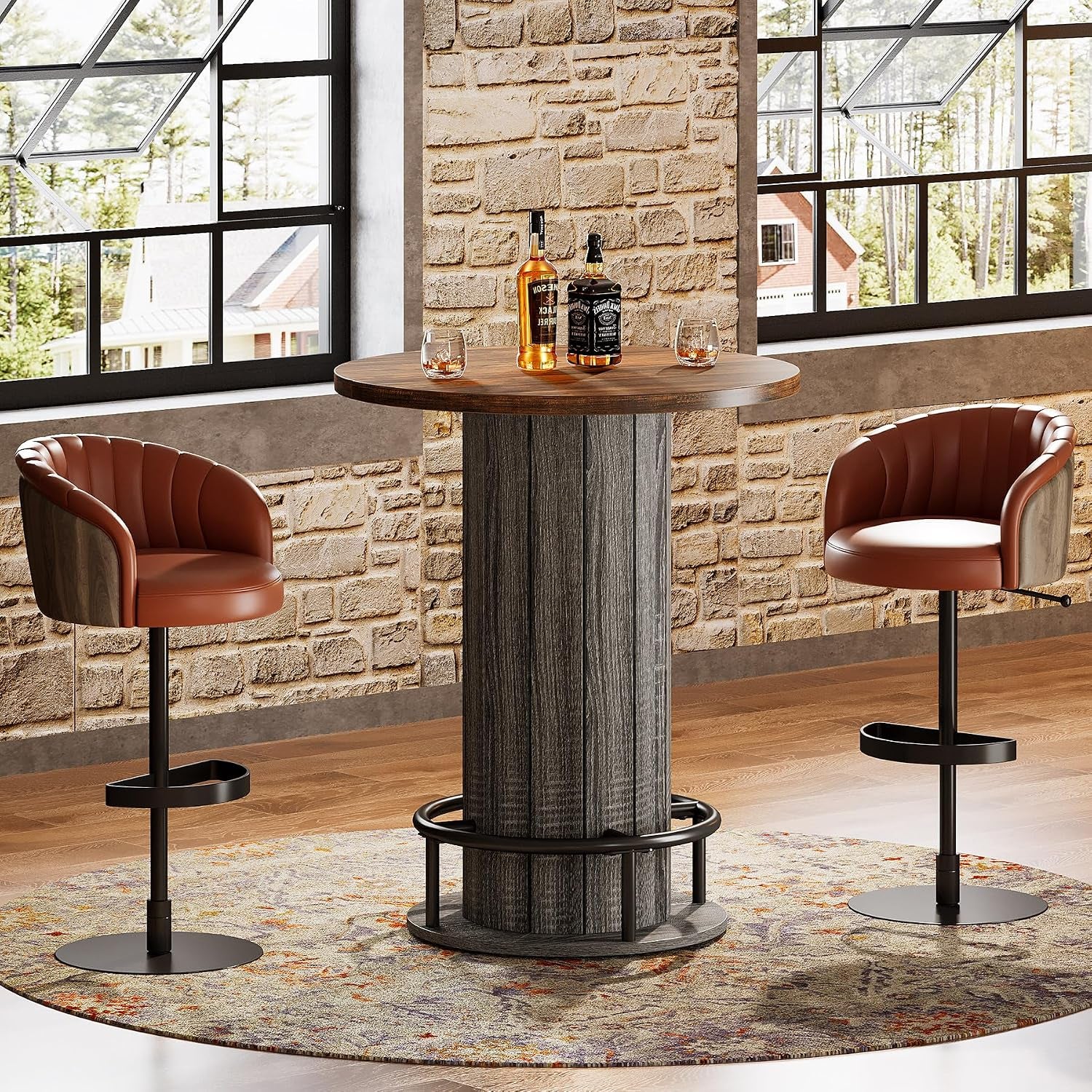Single round table shown against a stone wall and large windows, bottles and glasses on the tabletop